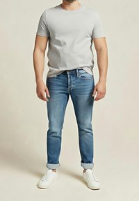 Světle šedé tričko s krátkým rukávem, střih na tělo; modré džíny s vybledlými detaily; bílé tenisky; ležérní outfit na mužském modelu.