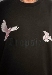 Fekete pamut póló, amelyen két fehér madár repül, valamint a "Dropsize" felirat sötét nyomtatással a mellkas területén.