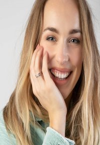 Zilveren ring met een verweven ontwerp gedragen aan een hand, vergezeld door een lachende vrouw met lang, golvend blond haar en een heldere huid.