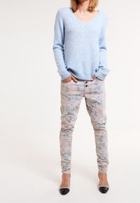 Ljusblå v-ringad tröja med långa ärmar, tillsammans med byxor i blommönster i pastellfärger och svarta spetsiga klackskor.