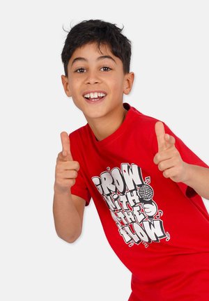 Rotes Baumwoll-T-Shirt mit einem grafischen Druck, auf dem der Text "WACHSE MIT DEM FLUSS" und ein Mikrofon abgebildet sind, getragen von einem Kind, das mit Daumen hoch gestikuliert.