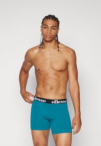 Türkise Boxershorts mit einem schwarzen elastischen Bund, der das Logo "ellesse" in Weiß zeigt. Glattes Material mit passgenauer Form.