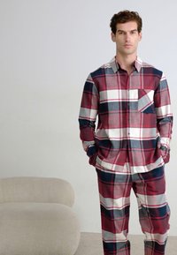 Conjunto de pijama de cuadros para hombre hecho de algodón. Esquema de colores en rojo, gris y azul marino con una camisa de botones, bolsillo en el pecho y pantalones a juego que presentan un patrón de cuadros.