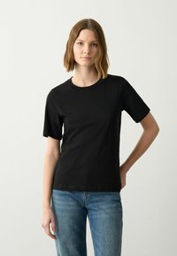 Zwarte katoenen T-shirt met een ronde halslijn en korte mouwen. Beschikt over een rechte snit en een subtiele brandingdetail aan de zijkant nabij de zoom.