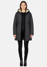 Zwarte geïsoleerde jas met een ritssluiting aan de voorkant, capuchon en twee zijzakken. Heeft een lichtgekleurde voering en reikt tot halverwege de dijen. Draagt over zwarte broek.