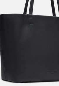 Czarna skórzana torba tote o gładkiej fakturze, z dwoma uchwytami na ramię oraz wytłoczonym logo u podstawy. Posiada minimalistyczny design i klasyczny kształt.
