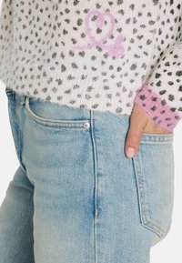 Strickpullover mit weißem Grund und schwarzen Punkten, bestickt mit einem rosa Herz. Kombiniert mit hellblauen Jeans aus Denim, die über normale Taschen verfügen.