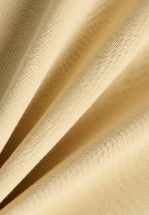 Close-up van zachte, beige gebreide stofplooien die een fijne textuur tonen, met diagonale schaduwen die diepte en detail versterken.