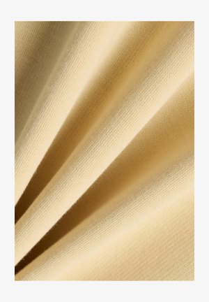 Close-up van zachte, beige gebreide stofplooien die een fijne textuur tonen, met diagonale schaduwen die diepte en detail versterken.