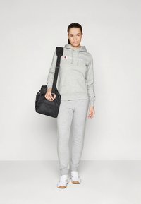 Grå fleece-hettegenser med logo, matchende grå joggebukser og hvite joggesko. Svart duffelbag med skulderstropp. Enkel, avslappet treningsklær.