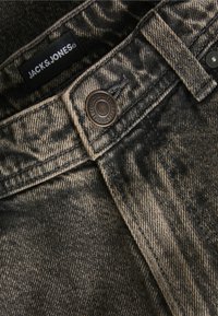 Μαύρα και γκρι τζιν παντελόνια με πλυμένη υφή, διαθέτουν μεταλλικό κουμπί και ορατές ραφές. Η ετικέτα γράφει "JACK & JONES."