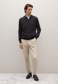 Dunkelgraues Polohemd mit langen Ärmeln und Kragen, kombiniert mit beigen Hosen. Dazu schwarze Slipper getragen. Einfaches und sauberes Design.