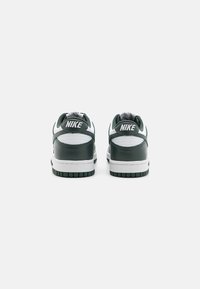 Des sneakers Nike verts et blancs présentent un extérieur en cuir lisse, un col rembourré et une semelle en caoutchouc texturée avec un motif de profil.