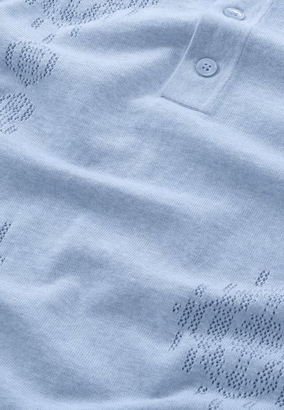 Vaaleansininen neulottu poolopaita, jossa on kaksi nappia, ja joka esittelee teksturoitua kuvioita sekä hienovaraisia avoimia ompeleita kankaan pinnalla.