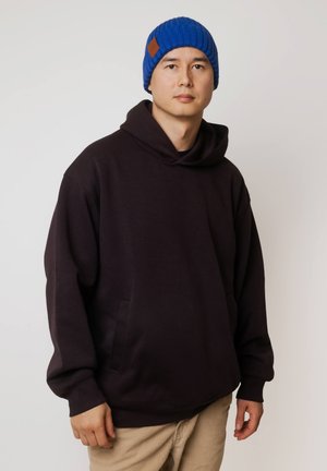 Ciemnofioletowa bluza z kapturem o luźnym kroju i przednią kieszenią. W zestawie z niebieską dzianinową czapką z brązową skórzaną naszywką.