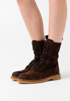 Bottes à lacets en daim marron avec une semelle en caoutchouc, dotées d'un bout arrondi, d'un tissu texturé et d'un détail zippé sur le côté.