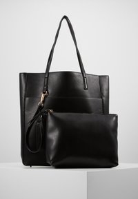 Sac fourre-tout en cuir noir avec deux longues anses, présentant un design élégant et une texture lisse. Comprend une petite pochette assortie avec fermeture éclair.