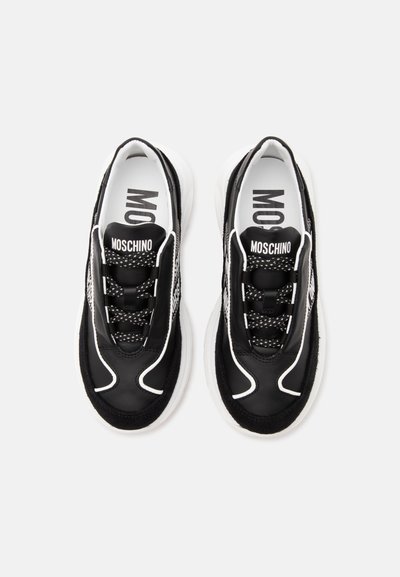 Paire de baskets Moschino noires et blanches avec des lacets à motifs, un marquage audacieux sur la languette et le côté, et des semelles blanches épaisses, vues de dessus.