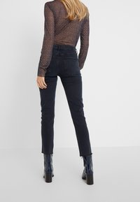 Jeans de mezclilla negros con corte slim y dobladillo deshilachado, combinados con una blusa transparente de manga larga con estampado floral. Presentan cintura alta y bolsillos traseros.