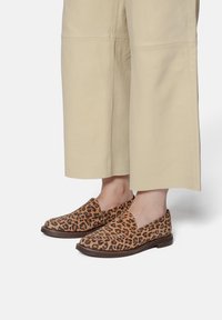 Cipele na vezanje s tkanjem leoparda i smešnim smeškom, upotpunjene glatkim bež širokim hlačama, koje prikazuju opuštenu siluetu.
