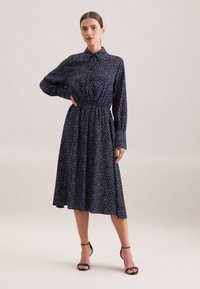 Vestito lungo a maniche, colore navy, con pois bianchi, colletto, vita elastica, gonna a campana, abbinato a sandali neri con cinturini alti.