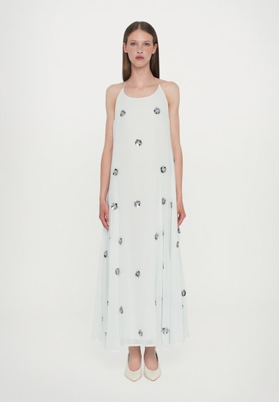 Vestido blanco fluido sin mangas con adornos florales plateados. Tejido ligero, silueta relajada, dobladillo a la altura de la rodilla. Combinado con tacones beige.