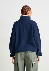 Pullover in pile di colore blu navy con colletto alto, vestibilità comoda e superficie texturizzata. Presenta un rivestimento verde a contrasto sul colletto.