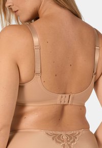 Béžová podprsenka s nastavovacími ramínky, hladkým povrchem a zapínáním na háček a očko na zadní straně. Bezšvový design s minimálním zdobením.