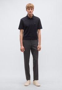 Tengerészkék rövid ujjú galléros póló, háromgombos patenttal és hímzett logóval, szénszürke szabott nadrággal és világos színű sportcipővel párosítva.