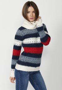Pull à col roulé rayé avec des nuances de marine, rouge et gris. Fabriqué à partir d'un matériau moelleux, avec un ourlet côtelé et de nombreux détails texturés.