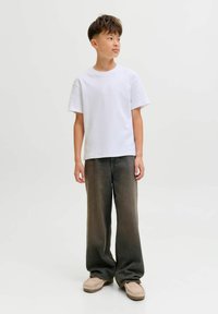 Bijela pamučna majica s kratkim rukavima, uparena s tamnim širokim trapericama. Obuća je u svijetlosmeđoj boji s teksturiranim detaljima.