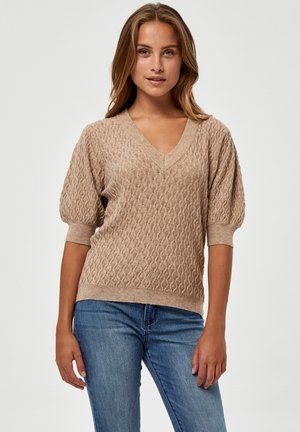 Beige pletený svetr s výstřihem do V, texturovaným vzorem, krátkými nabíranými rukávy a elastickými manžetami. V kombinaci s modrými džíny.