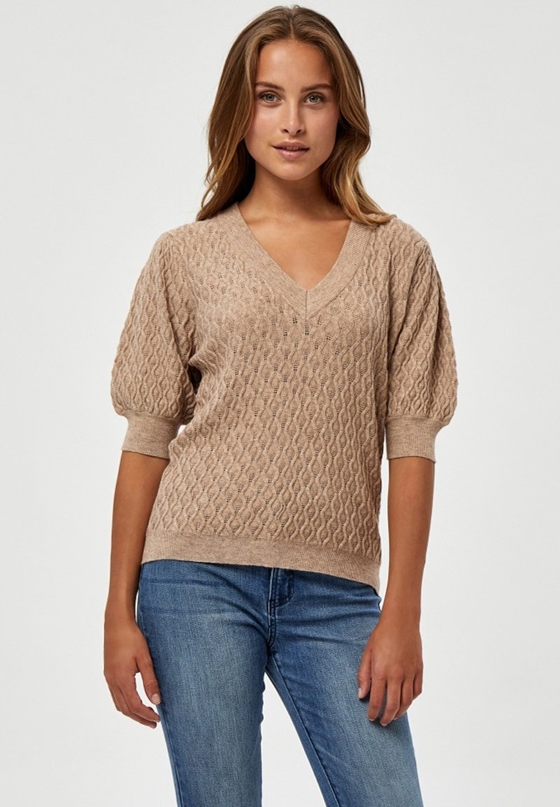 Beige pletený svetr s výstřihem do V, texturovaným vzorem, krátkými nabíranými rukávy a elastickými manžetami. V kombinaci s modrými džíny.