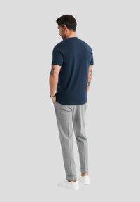 T-shirt in cotone blu navy con colletto a girocollo, abbinato a pantaloni grigi chiari su misura e sneaker bianche, visto da dietro.