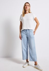 Haut blanc à manches courtes, pantalon large bleu clair et baskets blanches. Tissu texturé avec une coupe décontractée et une taille élastique.