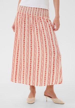 Femme portant une jupe midi crème avec des rayures florales verticales orange, associée à des chaussures tissées crème à talon et dos ouvert.