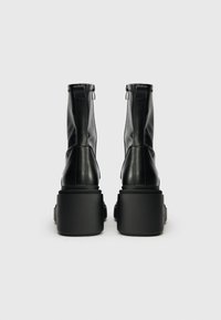 Bottines en cuir noir avec une finition lisse. Présentent une semelle plateforme épaisse et une fermeture éclair à l'arrière. Design minimaliste avec des coutures verticales.
