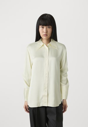 Light yellow satin blouse with a pointed collar, button-down front, and long sleeves. Smooth texture; slightly loose fit.