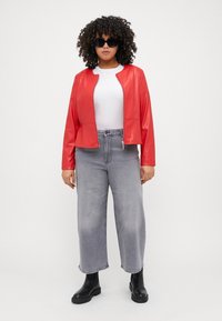 Κόκκινο τεχνητό δέρμα μπουφάν με φερμουάρ μπροστά, συνδυασμένο με ψηλόμεσα, φαρδιά γκρι τζιν και μαύρες μπότες Chelsea. Μαύρα γυαλιά ηλίου.