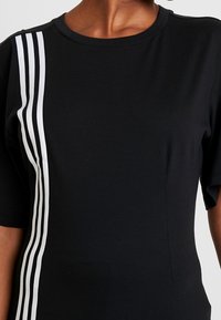 Czarna koszulka z krótkim rękawem i okrągłym dekoltem, z trzema pionowymi białymi paskami wzdłuż lewej strony. Wykonana z gładkiego materiału bawełnianego.