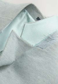 Hellgrau strukturierter Blazer mit hellblauem gemustertem Innenfutter, das am Kragen und innen am Jackett sichtbar ist.