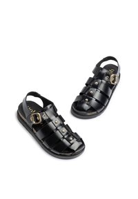 Sandalias negras con un diseño trenzado, tiras anchas, hebilla lateral, acentos dorados y suela acolchada. Acabado texturizado en las tiras.