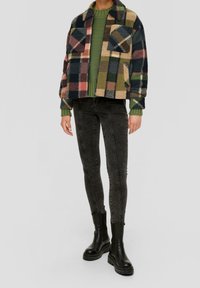 Chaqueta de forro polar de cuadros con dos bolsillos, en colores azul marino, verde y rosa. Combinada con jeans oscuros ajustados y botas negras gruesas.
