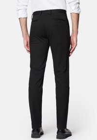 Czarne, dopasowane spodnie o gładkiej fakturze, z dwoma tylnymi kieszeniami zapinanymi na guziki oraz subtelnymi akcentami w postaci szwów, noszone z czarnymi butami.