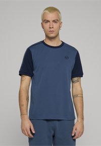 Niebieski T-shirt z krótkim rękawem z granatowymi akcentami, okrągłym dekoltem i małym logo na piersi. Gładka tekstura i luźny krój.