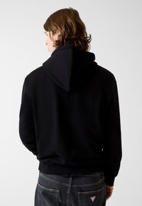 Czarna bluza z kapturem o miękkiej teksturze, z prążkowanymi mankietami i ściągaczem u dołu. Posiada kieszeń kangurka i minimalistyczny design, noszona z ciemnymi jeansami.