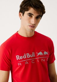 Rød bomulds t-shirt med et gråt "Red Bull Racing" logo og okse grafik, rund hals og korte ærmer.