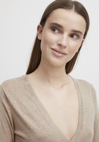 Pull en V beige avec une texture douce, arborant un col côtelé et une coupe décontractée, présenté sur un fond neutre.