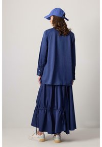 Navyblauwe jurk met lange mouwen en gegolfde manchetten, gelaagde rok met geplooide details, gecombineerd met een bijpassende blauwe pet en sneakers.