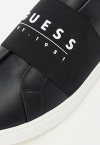 Sneaker nera con punta in pelle liscia, fascia elastica con logo bianco "GUESS" e suola in gomma testurizzata.